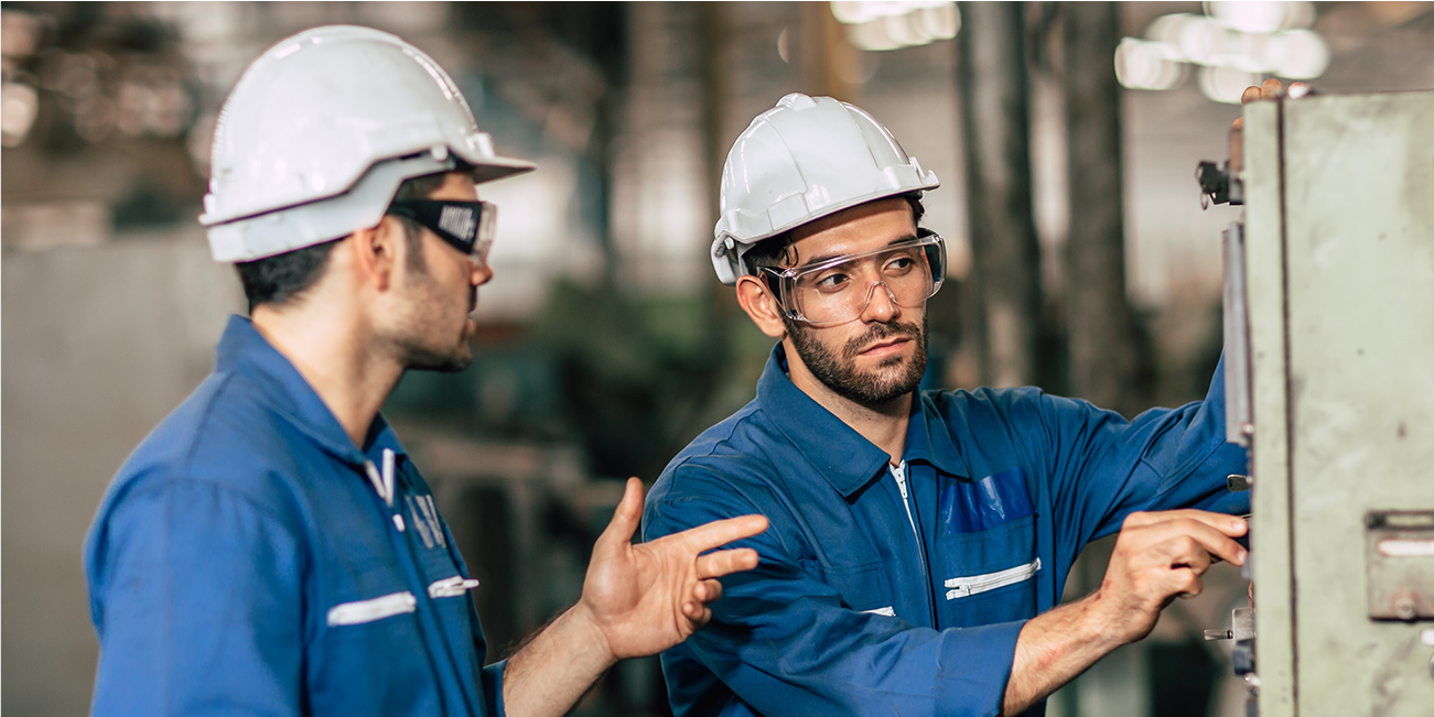 Two manufacturing workers in safety gear examining a switch box.