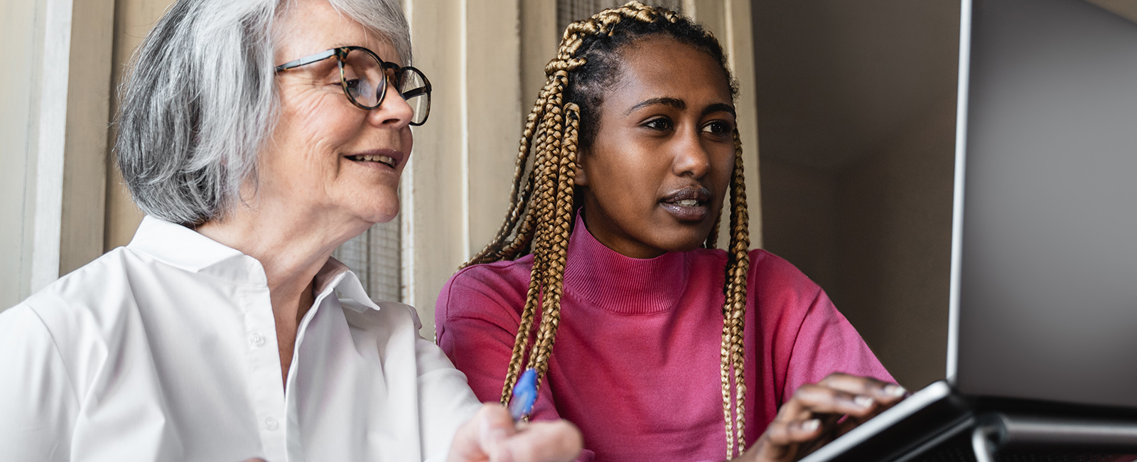 A younger woman and older woman look at a laptop screen together.