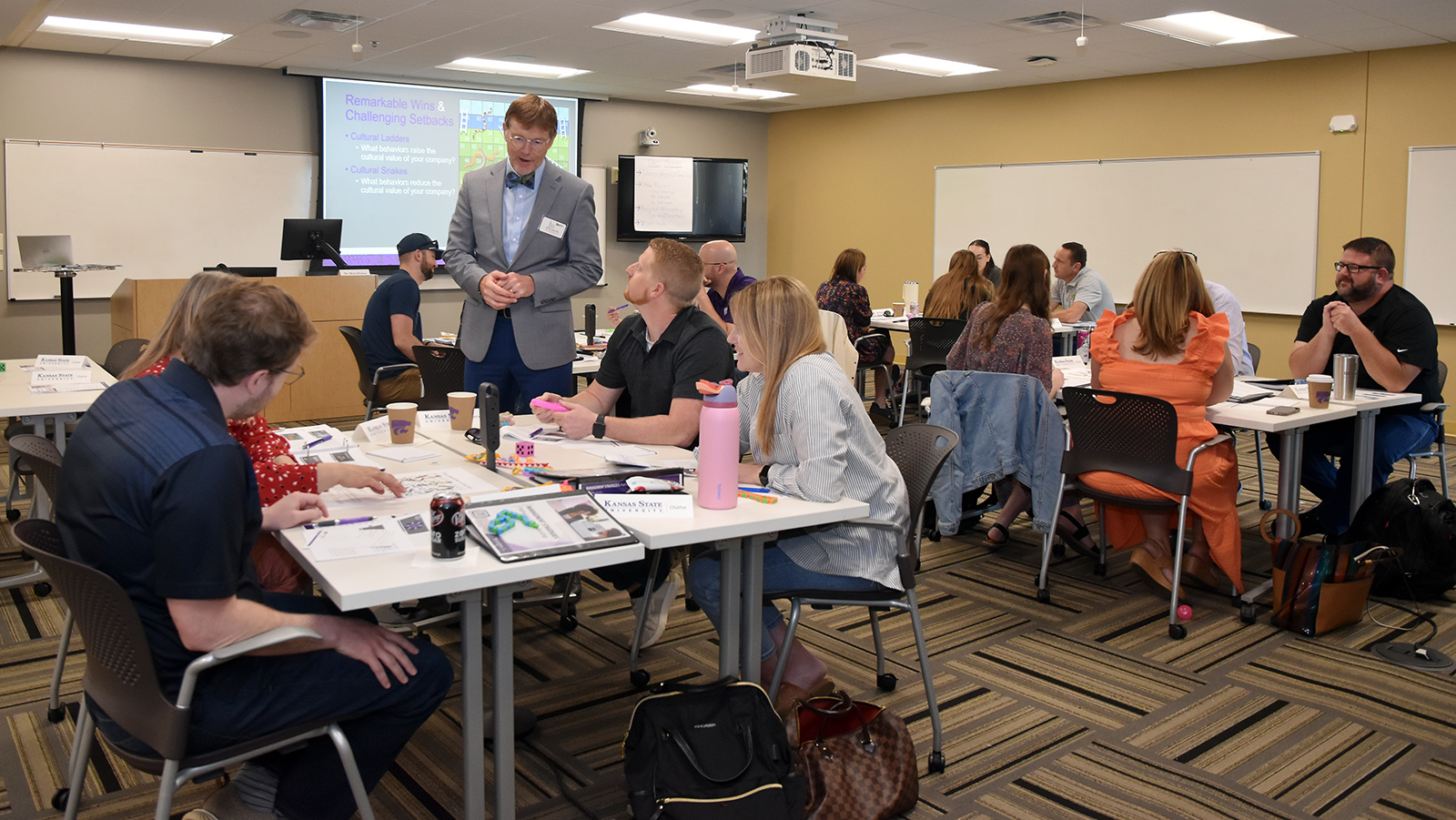 Leadership instructor with a bow tie walking around a classroom of adult learners. Leadership instructor with a bow tie walking around a classroom of adult learners.